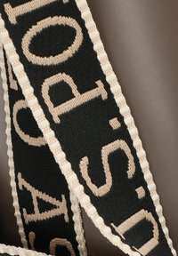 Correa negra con texto tejido en beige, acabado texturizado y detalles en blanco a lo largo de los bordes, mostrando un diseño tipográfico audaz.