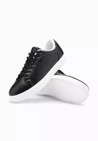 Baskets en cuir noir avec semelles en caoutchouc blanches, dotées d'un bout rond, d'un laçage à l'avant et d'accents texturés. Design minimaliste avec un col rembourré.