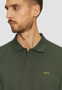 Ciemnozielona koszulka polo wykonana z teksturowanej tkaniny, z kołnierzykiem, dwoma guzikami i małym złotym logo "s.Oliver" na piersi.