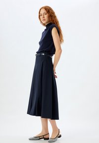 Top senza maniche blu navy con collo alto, abbinato a una gonna midi blu navy fluida e scarpe slingback nere con dettaglio in argento sulla punta.