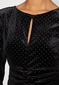 Robe en velours noire avec un décolleté en forme de goutte d'eau et des clous argentés dispersés, avec des détails froncés à la taille.