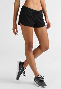 Svarta löpartights med nätstruktur, dragsko i midjan och sidofickor, i kombination med svarta och vita mönstrade sportskor.