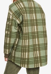 Zeleno-béžová kostkovaná nadměrná bunda z měkké vlněné látky, s oblým lemem a žebrovanými manžetami. Výrazná díky svému kostkovanému vzoru.