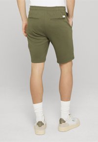 Shorts en coton vert olive avec une taille élastique, deux poches arrière et une texture lisse, associés à des chaussettes blanches et des baskets décontractées.
