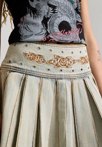 Denim pleated skirt with grommets and embroidered rose pattern at the waistband, worn with a black dragon graphic t-shirt.