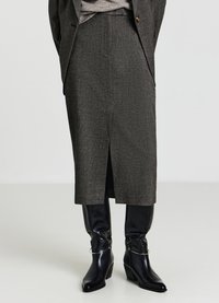 Gonna midi grigia in tessuto strutturato, caratterizzata da uno spacco frontale. Abbinata a stivali neri al ginocchio con tacco e dettagli metallici.