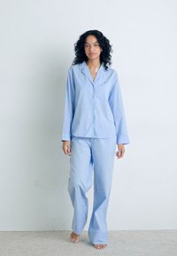 Blå och vit randig pyjamasuppsättning med en knapp-up långärmad skjorta och avslappnade byxor, tillverkad av mjukt tyg.