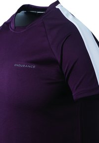 Lilla træningsskjorte med korte ærmer og hvide sideaccenter. Materialet har en glat tekstur med "ENDURANCE" logoet på forsiden.