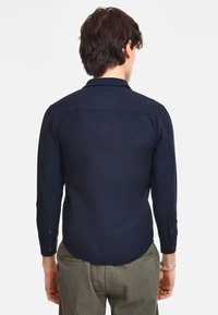 Maglietta a manica lunga blu navy con colletto classico, polsini con bottoni e orlo svasato, caratterizzata da una texture liscia e dettagli di cucitura minimi.