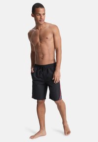 Μαύρο μαγιό σορτς με ελαστική μέση και κορδόνι. Διαθέτει αντίθετο μοτίβο με κόκκινες ρίγες στα πλαϊνά. Ελαφρύ, κοντό σχέδιο.