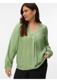 Blouse ample vert clair avec un col en V et des manches longues. Texture douce et poignets élastiques. Aucun motif ni détail métallique visible.