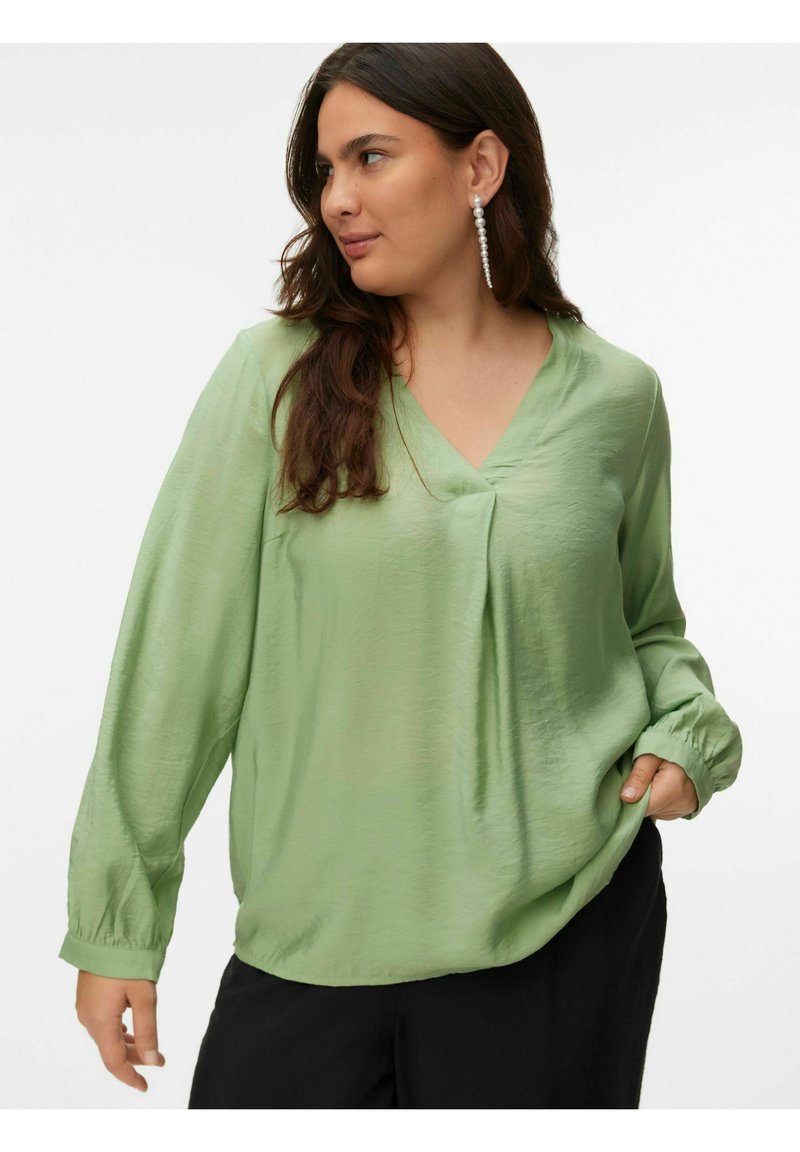 Blouse ample vert clair avec un col en V et des manches longues. Texture douce et poignets élastiques. Aucun motif ni détail métallique visible.