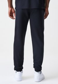 Tamno plave trenirke izrađene od mekanog materijala, s prilagođenim krojem, elastičnim manžetama i glatkom teksturom. Uparene s bijelom obućom.