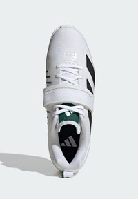 Hvide sportssko med sorte striber, mesh-overdel, forstærket tå og grønne detaljer. Har snøre og en rem for en sikker pasform.