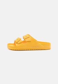 Sandale en caoutchouc jaune avec deux sangles à boucle réglables, semelle intérieure texturée et semelle extérieure striée pour une meilleure adhérence. Design simple et ouvert.
