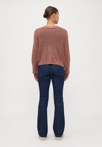 Suéter de punto, corto, en rosa empolvado, combinado con jeans acampanados de color azul oscuro. El conjunto presenta un acabado texturizado y un corte relajado.