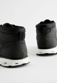 Czarne wysokie buty wykonane z materiału syntetycznego, z teksturowanym wykończeniem, wyściełanym kołnierzem i białą gumową podeszwą z wycięciami.