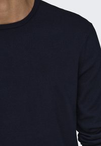 Pull à manches longues bleu marine avec col rond. Texture lisse avec poignets et ourlet côtelés, doté d'un design simple sans motifs ni accents.