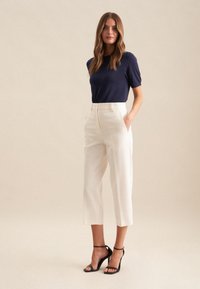Navy-blaues Kurzarmoberteil, kombiniert mit cremefarbenen, knöchellangen Hose und schwarzen Riemenabsätzen. Hat ein einfaches Design mit einer klassischen Silhouette.