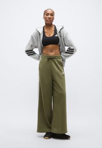 Sportowy strój obejmujący szarą bluzę z kapturem na zamek z czarnymi paskami, czarny stanik sportowy oraz oliwkowozielone spodnie dresowe o szerokich nogawkach. Czarne buty sportowe.