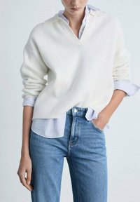 Jersey blanco con relieve y escote en V, con mangas extragrandes, superpuesto a una camisa de rayas azul claro, combinado con jeans azul claro.