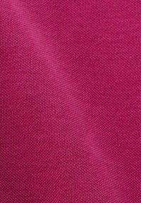 Gros plan sur un tissu tricoté texturé de couleur rose foncé, montrant un motif fin de tricot et un pli diagonal subtil.