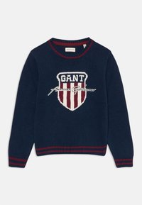 Maglione blu navy con logo a scudetto a righe rosse e bianche, testo "GANT American Sportswear" e polsini e orlo a coste a righe rosse.