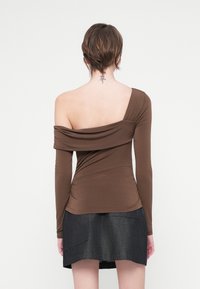 Hnědý dlouhý rukáv top s designem jednoho ramene a detailem nařasené tkaniny, spárovaný s tmavými džíny mini sukní. Hladká textura.