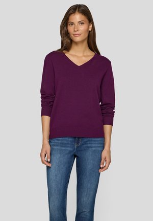 V-Ausschnitt lila Pullover aus weichem Material, mit langen Ärmeln und gerippten Bündchen, kombiniert mit blauen Jeans in lässiger Passform.