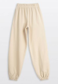 Beżowe dresowe spodnie z elastanem w pasie i na kostkach, w luźnym kroju, wyeksponowane na białym tle.