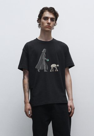 Sort bomulds t-shirt med grafik af en karakter i en kappe, der går med en lille robot. Korte ærmer, afslappet pasform.