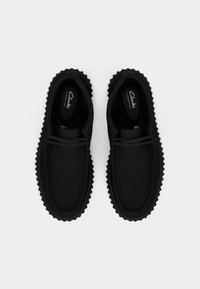 Scarpe in suede nero con forma arrotondata, suola in gomma con grip texturizzato e design con lacci. L'interno presenta il marchio Clarks.