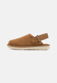 Bruna mockaskor med halkfri sula, slingback-design och en sidoknapp som accent. Texturerad ovandel med sömnad längs kanten.