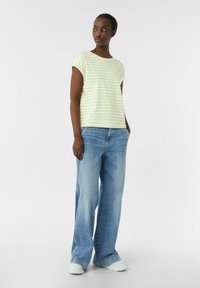 Gestreept T-shirt met korte mouwen van lichtgeel en witte stof, gecombineerd met losse blauwe denim jeans en witte sneakers. Eenvoudig ontwerp met opgerolde mouwen.