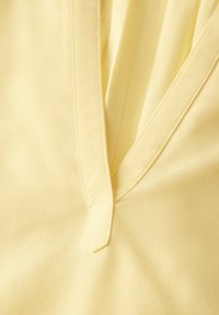 Il tessuto giallo presenta una consistenza morbida con un design a placca, cucito lungo i bordi e una finitura liscia.