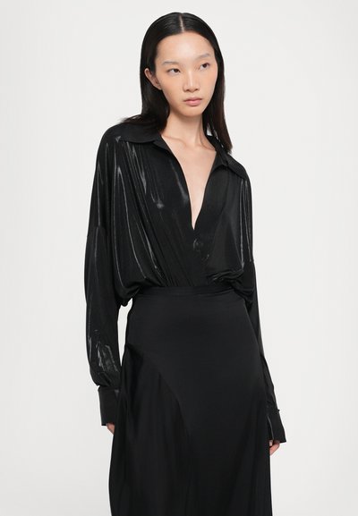 Black long-sleeve shirt with a deep v-neck, made of glossy fabric, paired with a smooth black skirt featuring an asymmetrical design.