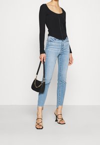 Sort ribbet langærmet top med en frontlynlås, lyseblå stramme jeans og en sort mini håndtaske med en gylden kæde. Sorte stiletter.