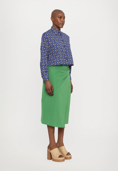 Blue and white patterned long-sleeve shirt, green wrap skirt, and beige clogs with wooden heels. Smooth textures and vibrant colors.