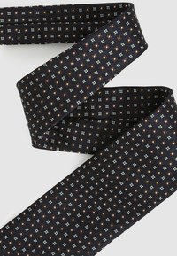 Cravat din țesătură țesută, cu o bază albastră închisă și modele geometrice în nuanțe de alb și marron. Textură moale și design plat.