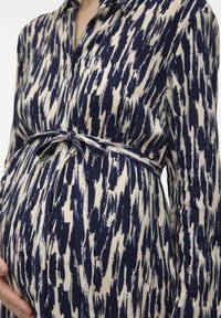 Gravidblus i krämfärg med marinblå abstrakta mönster, långa ärmar, knäppning fram och knytning i midjan som framhäver byst och mage.