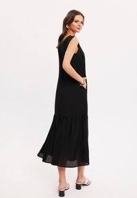 Czarna, bezrękawnikowa sukienka z poziomym dołem i subtelną teksturą. Ma boczne kieszenie oraz luźny krój. Połączona z jasnymi sandałami na grubym obcasie.