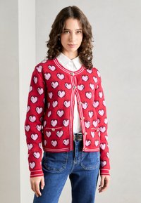 Punainen neulevillatakki, jossa on vaaleanpunaisia sydäntulostuksia, napitettavalla etuosalla, pyöreällä kaula-aukolla ja kontrastivalkoisilla reunuksilla. Kaksi etup distinctiä taskua.