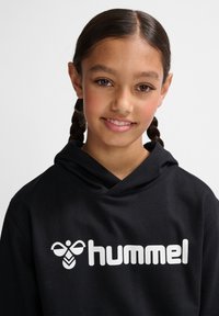 Schwarzer Hoodie mit einem großen weißen "hummel"-Logo und einer Bienen-Grafik auf der Brust. Weicher Stoff mit lockerer Passform und Kapuze.