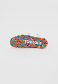 Bijela skateboard cipela s višebojnom uzorkastom gumenom potplatom. Ima hrabri "GLOBE" logo sa strane. Tekstura površine pruža dobar zahvat.
