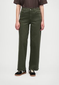 Olivově zelené kalhoty s širokými nohavicemi, vysokým pasem, pěti kapsami a jedním předním knoflíkem. V kombinaci s černými teniskami se bílým akcentem.