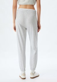 Lichtgrijze joggingbroek met een elastische tailleband en enkels, met een zachte stoftextuur en een relaxte pasvorm, gecombineerd met witte sneakers.