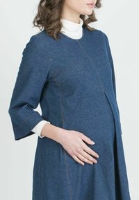 Raskahamama mehupuku tummansinisena, jossa on kolmivuoraiset hihat, pyöreä pääntie ja erottuva oranssi ompelu. A-linjainen malli mukavuutta varten.