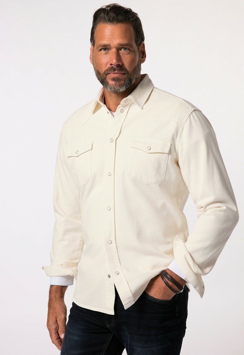 Kermanvärinen pitkähiha-paita, jossa painonapit, kaksi rintataskua ja kevyt tekstuuri. Hihat käärityt ylös, päällä tummansiniset farkut.