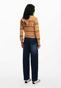 Randig hoodie i varma nyanser av orange och gult, i kombination med vida mörkblå denimjeans med bakfickor och sömdetalj.