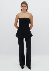 Černý top bez ramínek s přiléhavým živůtkem a rozšířeným lemem, kombinovaný s černými kalhotami s rovnými nohavicemi a lodičkami se špičatou špičkou.